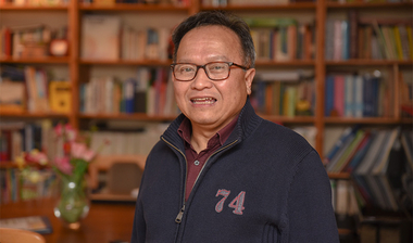 Dominic Sang Nguyen steht in seinem Wohnzimmer vor einer Bücherwand